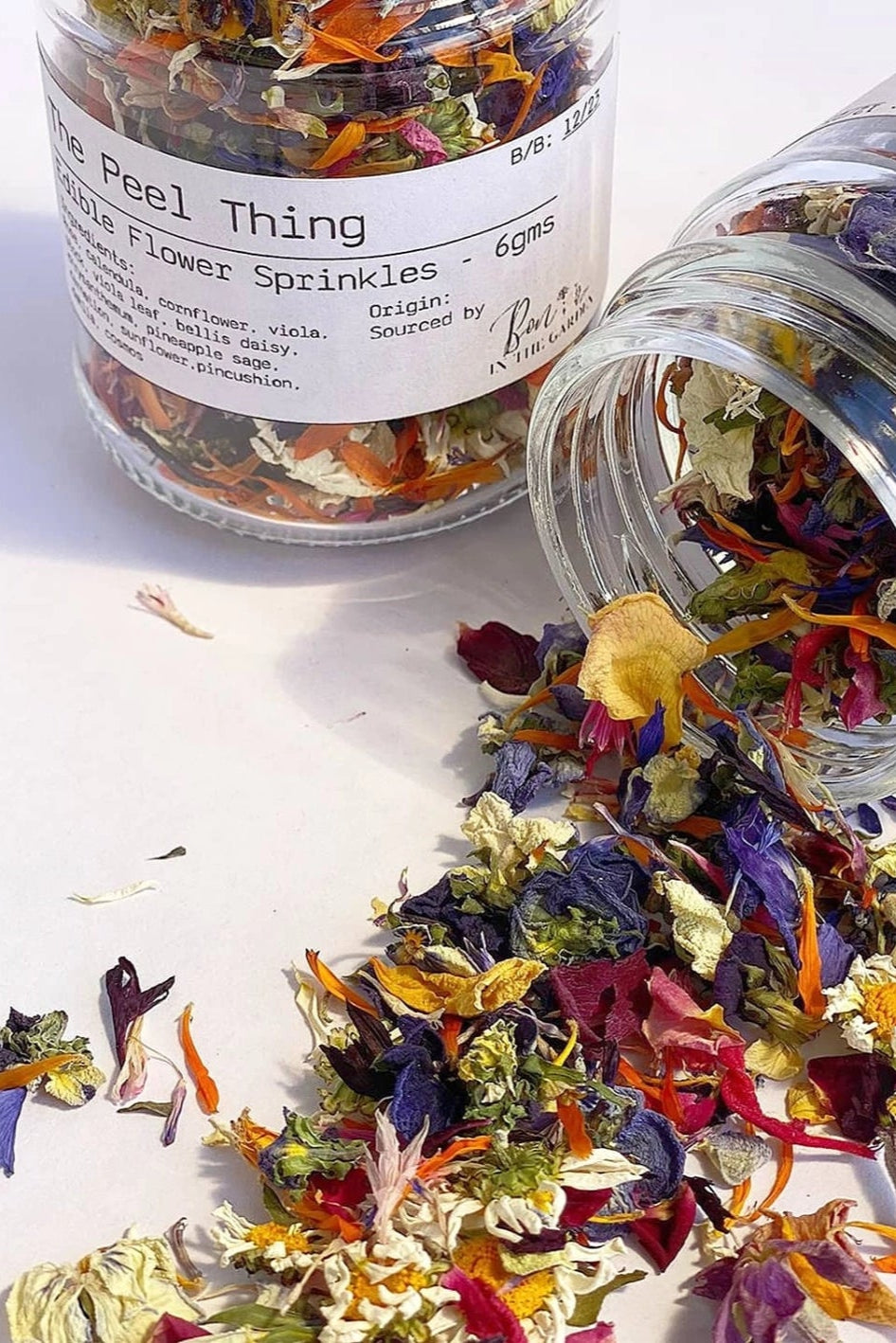 Colorful flower sprinkles spilling out of a jar labeled 'The Peel Thing' on a white background.